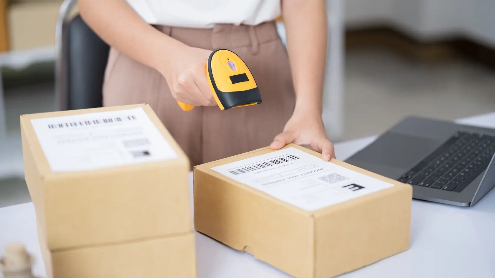 Hands scanning barcode on delivery parcel. Worker scan barcode of cardboard packages before delivery at storage. Woman working in factory warehouse scanning labels on the boxes with barcode scanner.